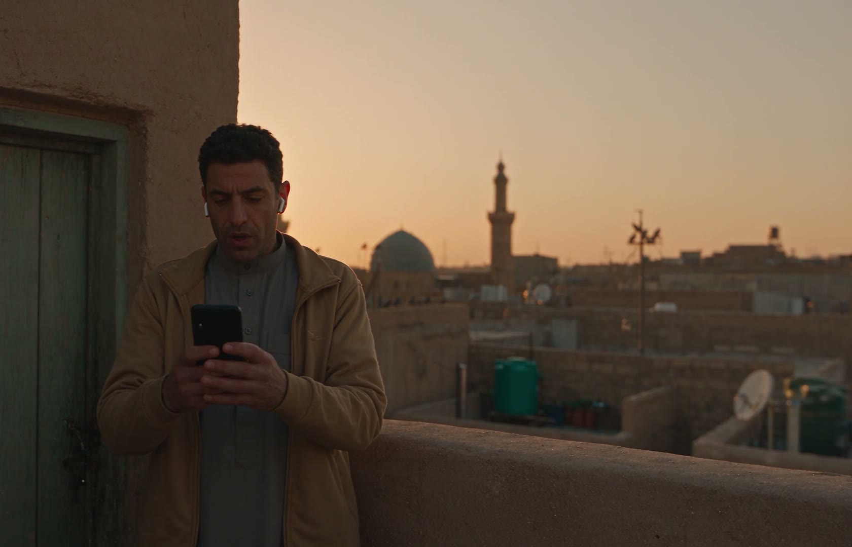 A man alone on a rooftop at dawn, reading his phone out of sight of the house