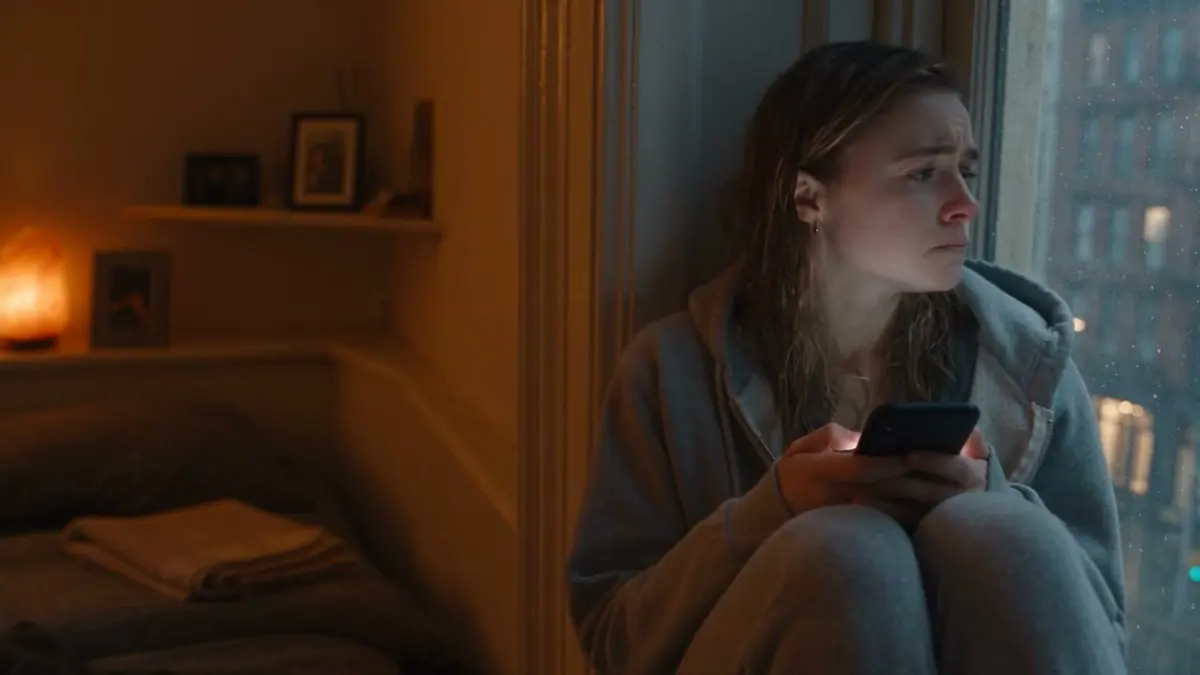 A woman in warm window light, reading her phone