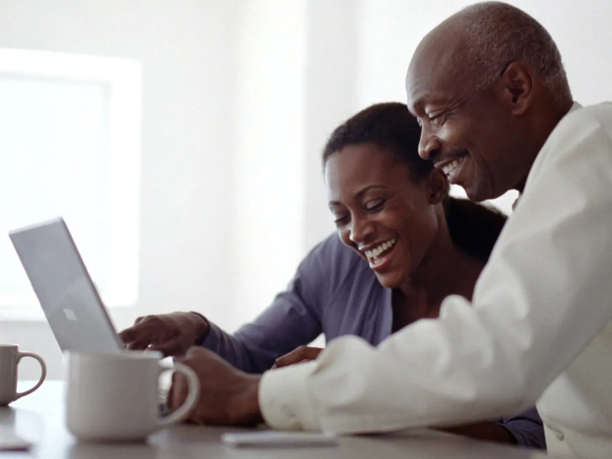 Three people laughing together over a laptop at a kitchen table